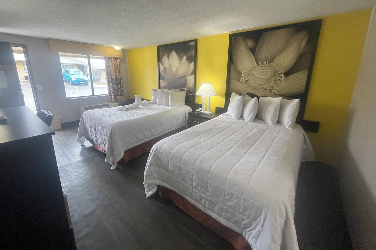 A hotel room with two beds, a desk, a lamp, and a large floral artwork on the wall.