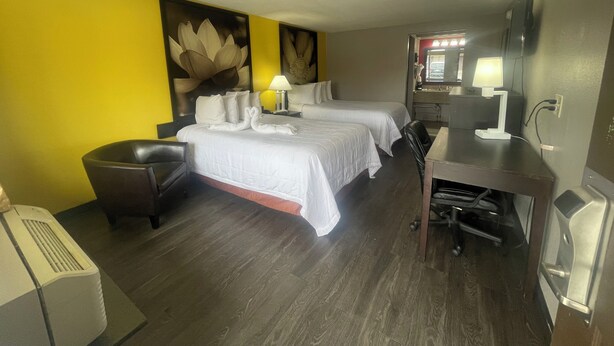 Habitación de hotel con dos camas, un escritorio, una silla, una lámpara de escritorio, un espejo y un aire acondicionado de pared.
