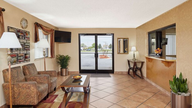 A hotel lobby with a seating area, a coffee table, a potted plant, a television, and a large window with a view of the parking lot.