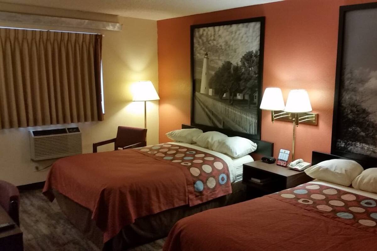 A hotel room with two beds, a desk, a chair, a lamp, and a large painting on the wall.