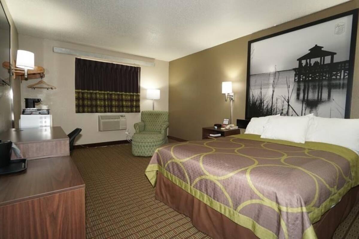 A hotel room with a large bed, a desk, a chair, a lamp, and a painting on the wall.