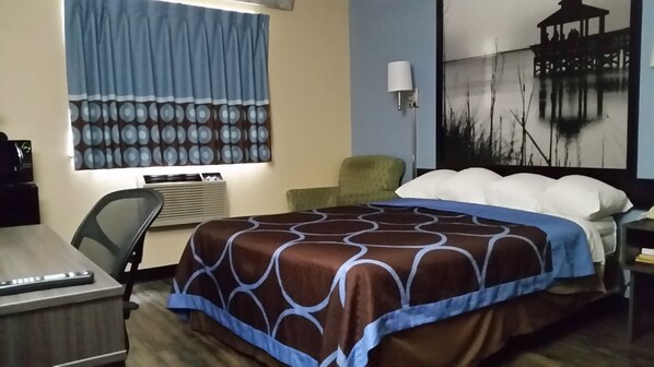 A hotel room with a bed, a desk, a chair, a lamp, and a painting on the wall. - Super 8 by Wyndham Greenville (Greenville)