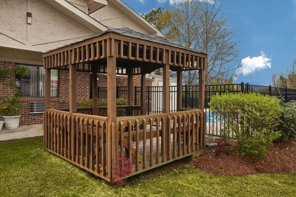 A wooden gazebo with a metal railing, surrounded by a brick building and a pool. - Super 8 by Wyndham Greenville (Greenville)