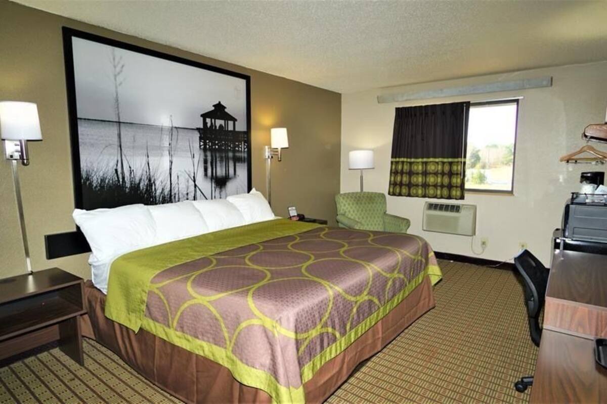 A hotel room with a large bed, a desk, a chair, a TV, and a window with curtains.