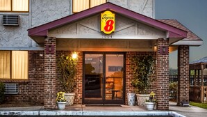 A hotel entrance with a prominent 'Super 8' sign, brick facade, and potted plants.