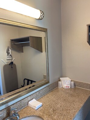 A bathroom with a mirror, sink, towel, and a towel dispenser. - Red Roof Inn Vero Beach - I-95 (Vero Beach)