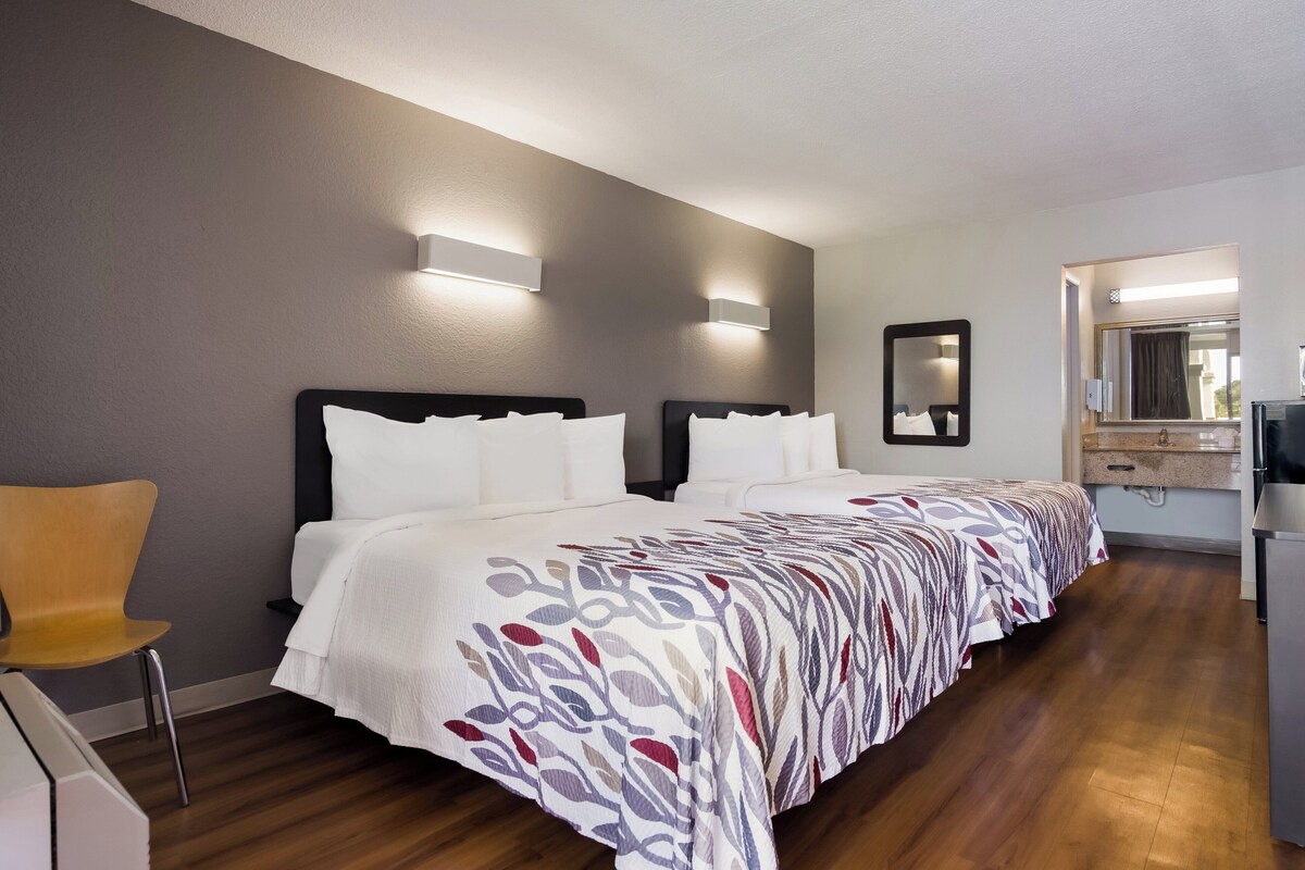 A hotel room with a large bed, two bedside tables, a chair, a mirror, and a small desk with a chair.