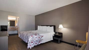 Habitación de hotel con cama, escritorio, silla, mesita de noche con lámpara y espejo.