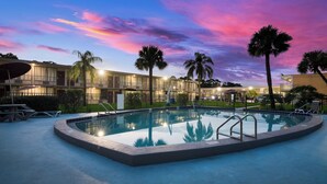 A swimming pool with a poolside area, palm trees, and a building with multiple balconies in the background. - Red Roof Inn Vero Beach - I-95 (Vero Beach)