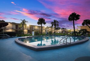 A swimming pool with a poolside area, palm trees, and a building with multiple balconies in the background. - Red Roof Inn Vero Beach - I-95 (Vero Beach)