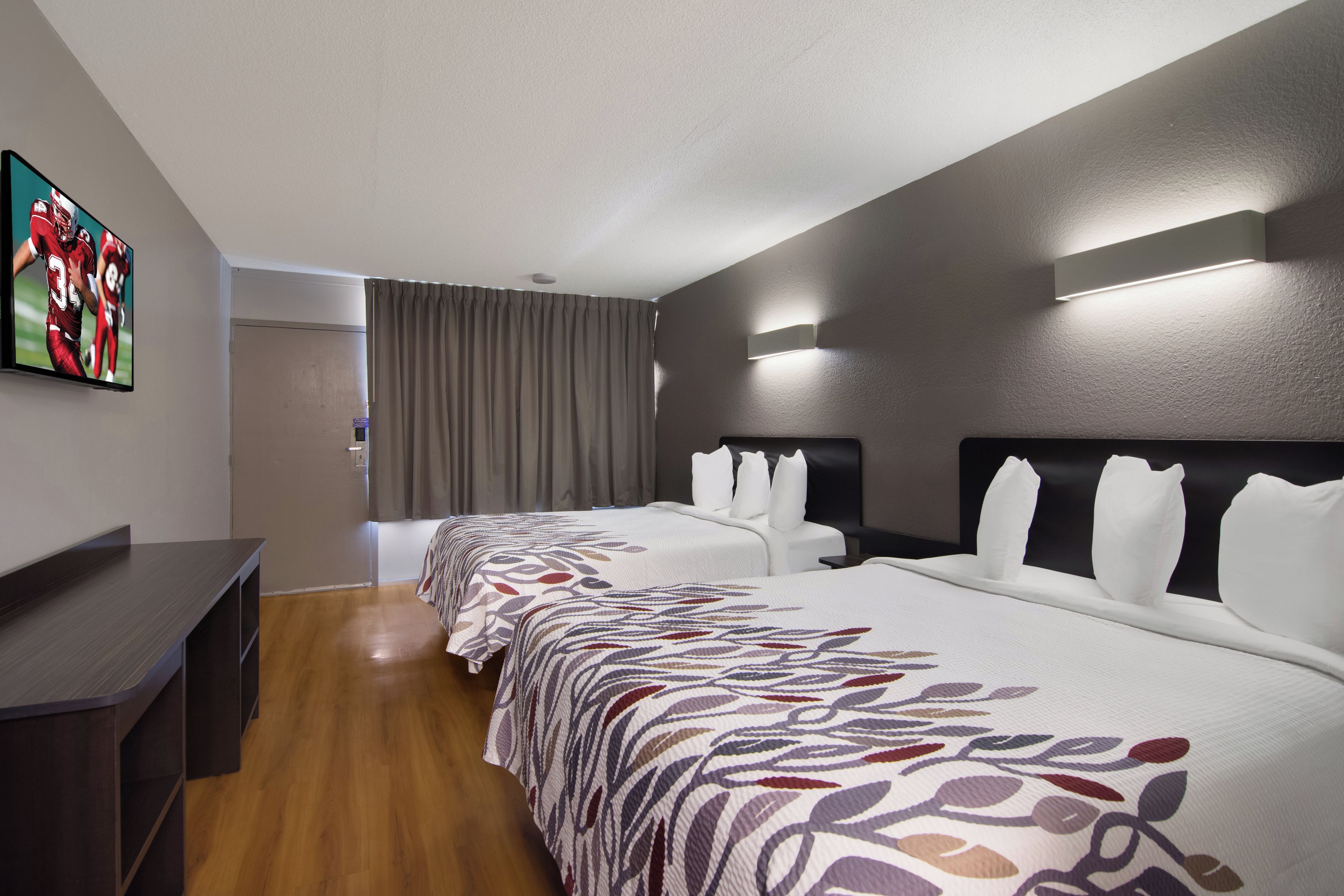 Una habitación de hotel con una cama grande, un escritorio y un televisor de pantalla plana montado en la pared.