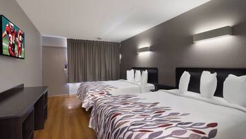 A hotel room with a long bed, a desk, and a flat-screen TV mounted on the wall.