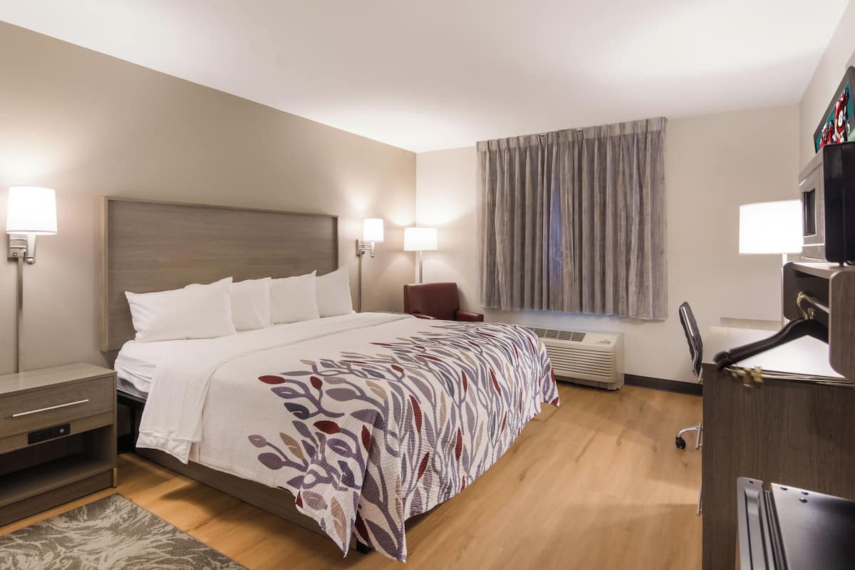 Habitación de hotel con cama, mesitas de noche, escritorio, silla, ventana con cortinas y aire acondicionado.