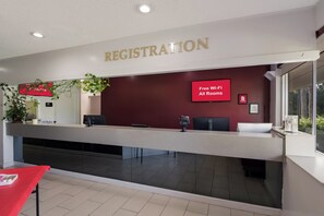 A hotel reception area with a registration desk, a sign indicating free Wi-Fi availability, and a window providing a view of the outdoors. - Red Roof Inn Vero Beach - I-95 (Vero Beach)