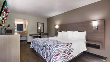 Habitación de hotel con una cama grande, un escritorio, una silla, un espejo y un televisor.