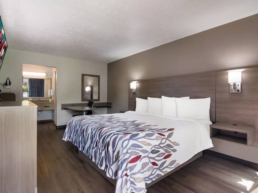 A hotel room with a large bed, a desk, a chair, a mirror, and a television.