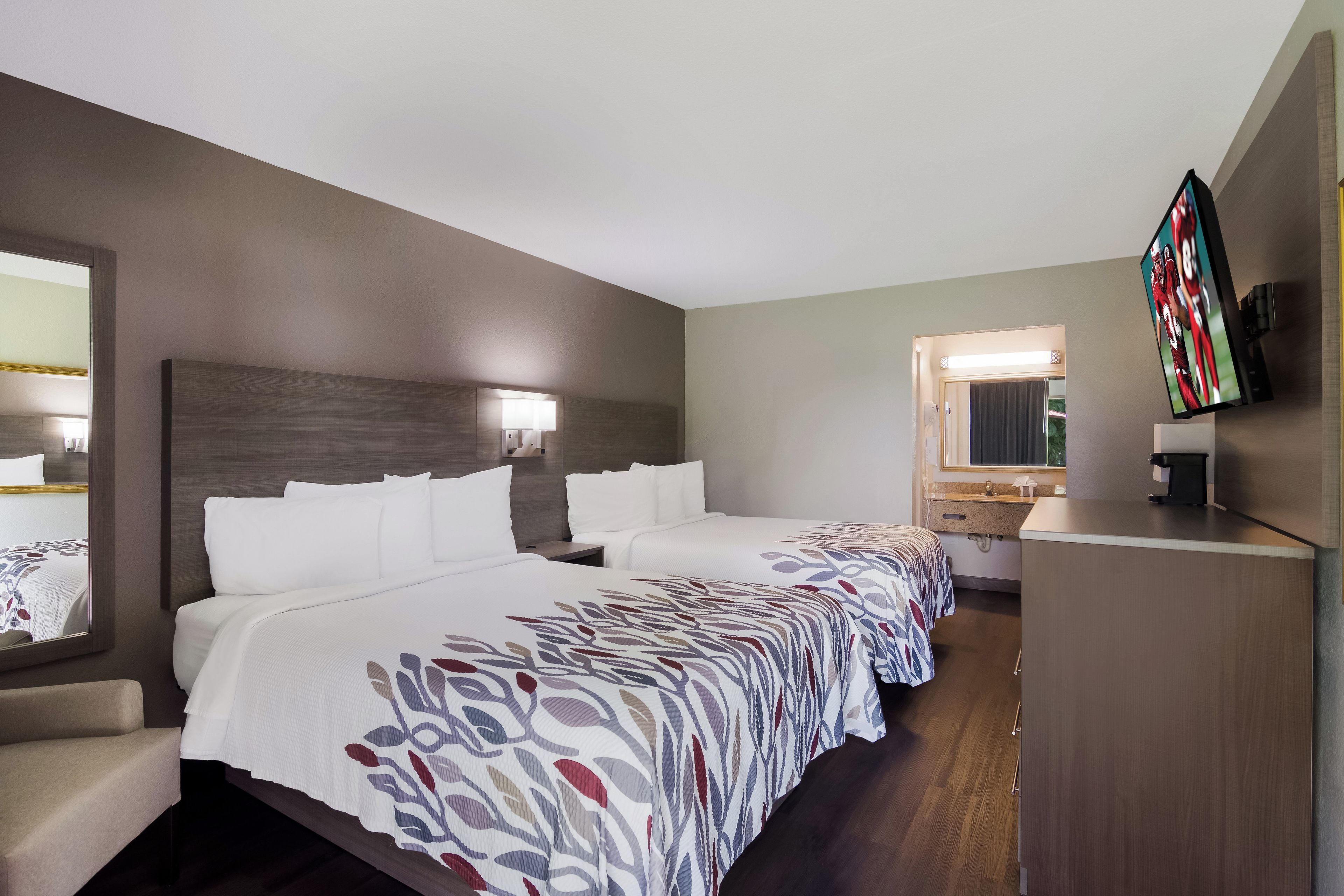 Habitación de hotel con dos camas, un escritorio, un espejo y una televisión.