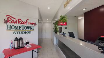 Un área de recepción con un letrero de Red Roof Inn, un mostrador de recepción, una estación de café y una planta.