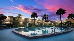 A swimming pool with a poolside area, palm trees, and a building with multiple balconies in the background. - Red Roof Inn Vero Beach - I-95 (Vero Beach)