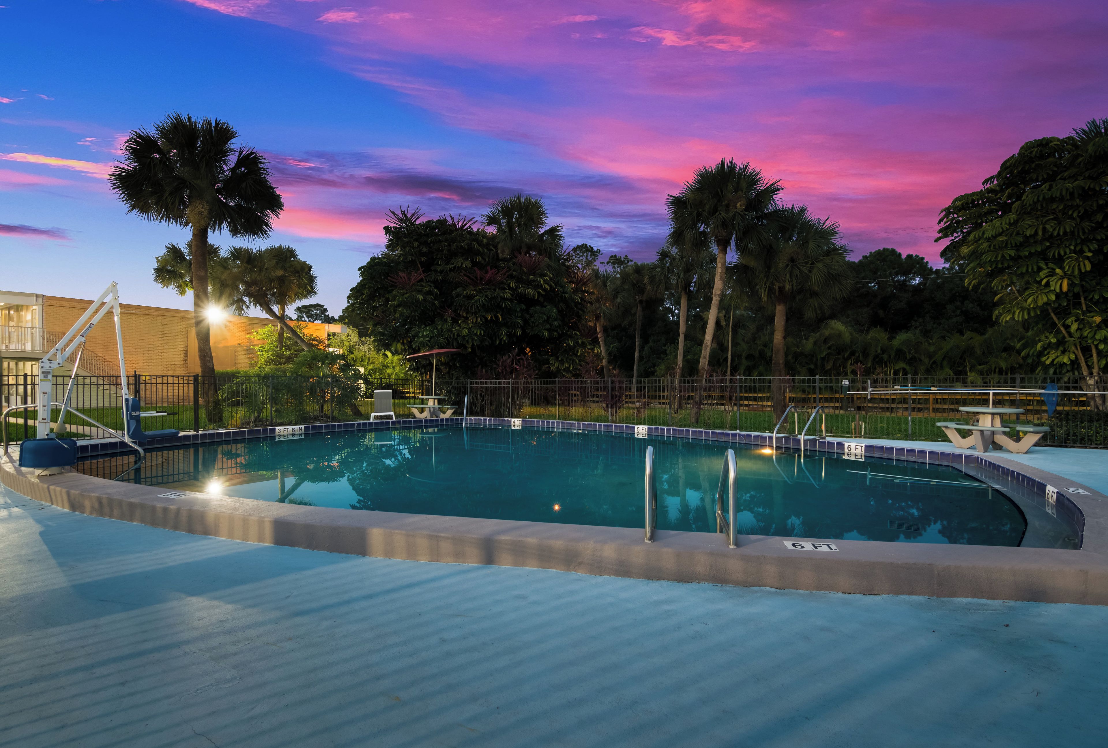 Una piscina con un deck circundante, palmeras y un cielo al atardecer.