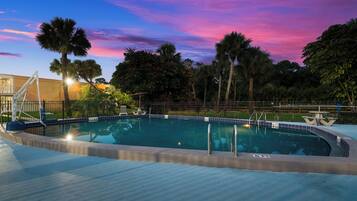 Una piscina con un deck circundante, palmeras y un cielo al atardecer.