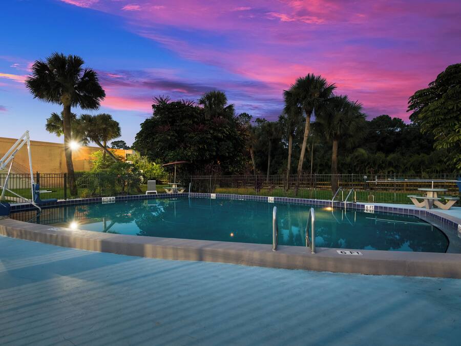 Una piscina con un deck circundante, palmeras y un cielo al atardecer.