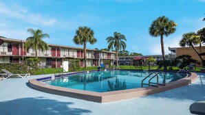A swimming pool with lounge chairs, palm trees, and a hotel building in the background. - Red Roof Inn Vero Beach - I-95 (Vero Beach)