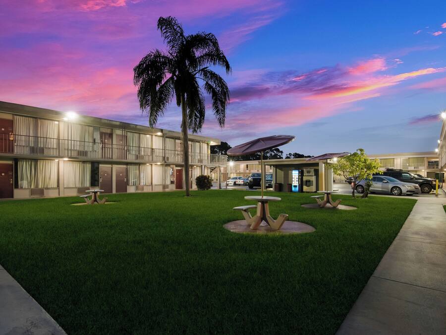 A hotel with a well-maintained lawn, outdoor seating, and a parking area.
