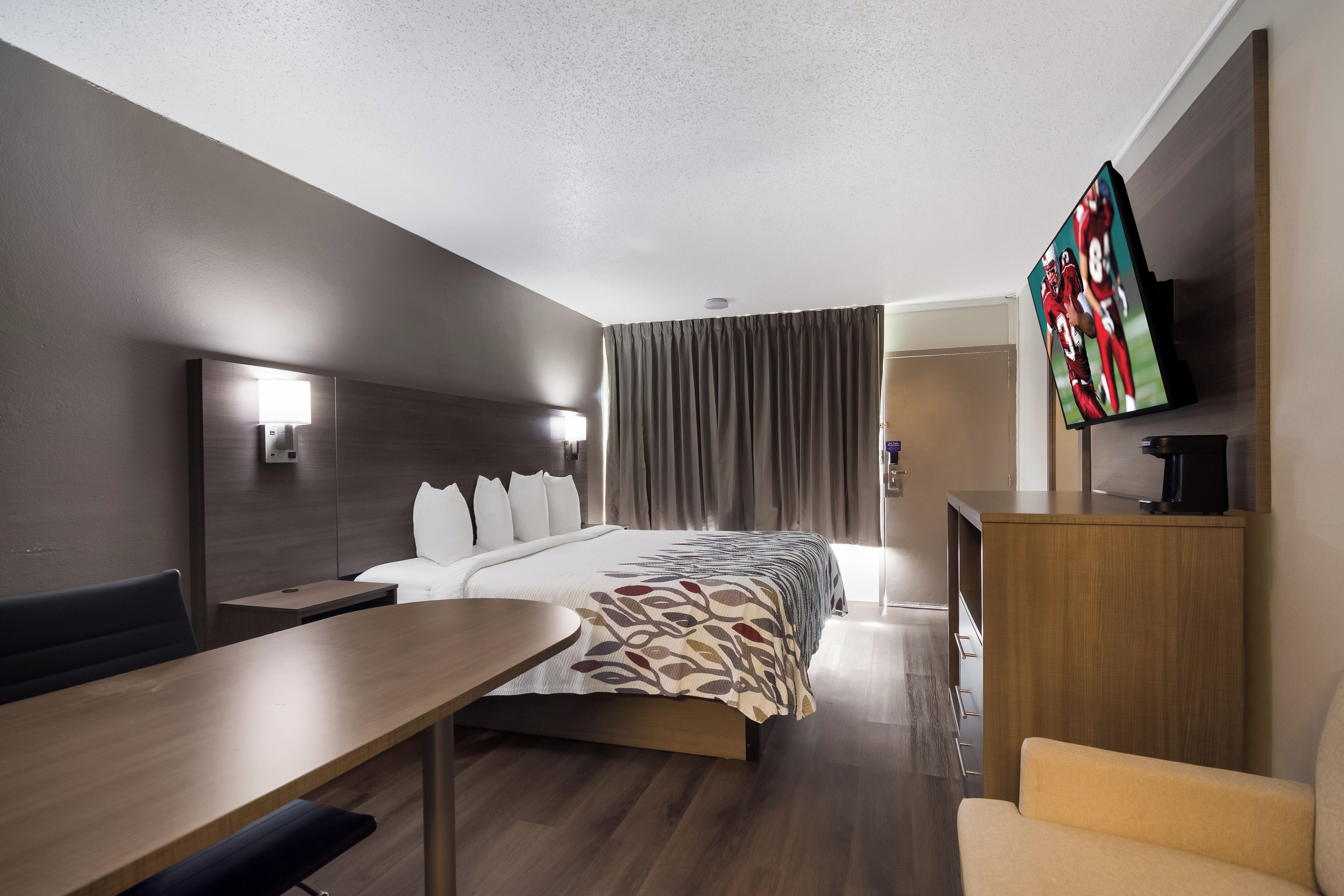 A hotel room with a bed, a desk, a chair, a TV, and a wardrobe.