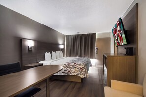 Ett hotellrum med en säng, ett skrivbord, en stol, en TV och en garderob.