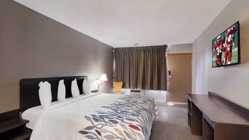 Habitación de hotel con cama, escritorio, silla, televisor y ventana con cortinas.