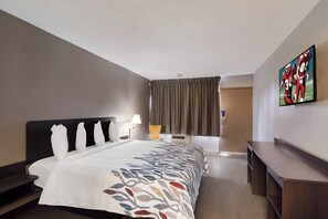 A hotel room with a bed, a desk, a chair, a TV, and a window with curtains. - Red Roof Inn Vero Beach - I-95 (Vero Beach)