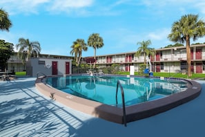 A swimming pool with a surrounding deck, palm trees, and a building with balconies in the background. - Red Roof Inn Vero Beach - I-95 (Vero Beach)