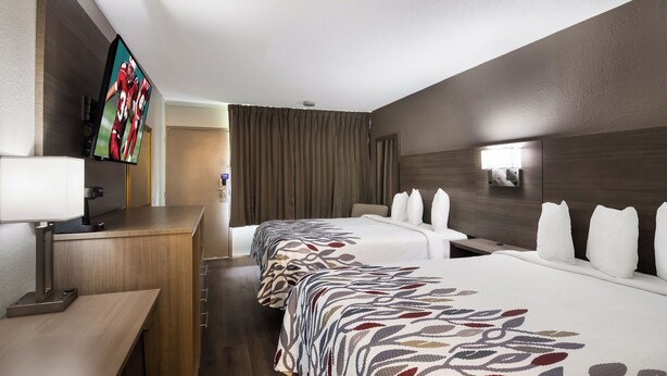 A hotel room with two beds, a desk, a TV, and a bathroom in the background. - Red Roof Inn Vero Beach - I-95 (Vero Beach)