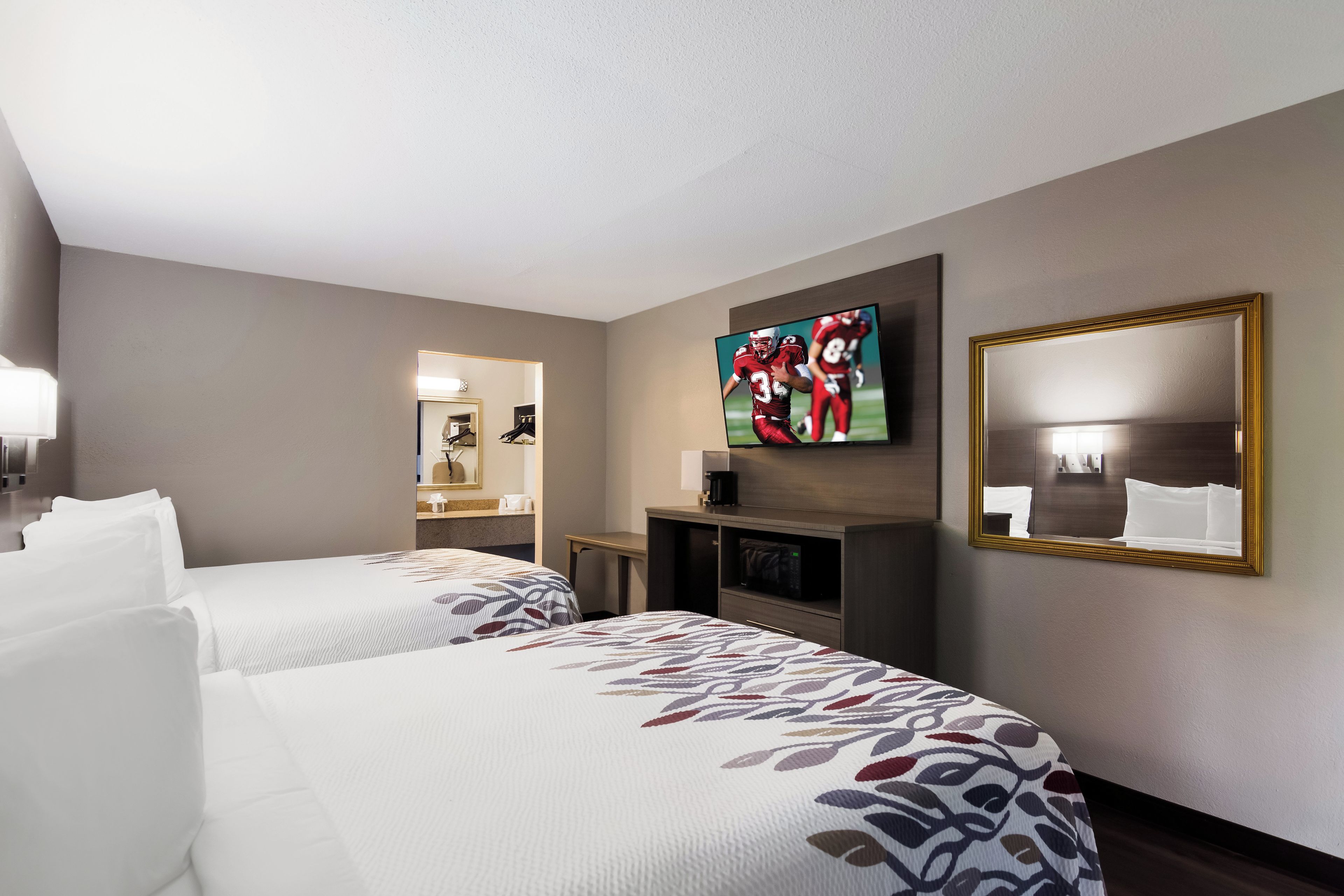 A hotel room with two beds, a television, a mirror, and a small table.