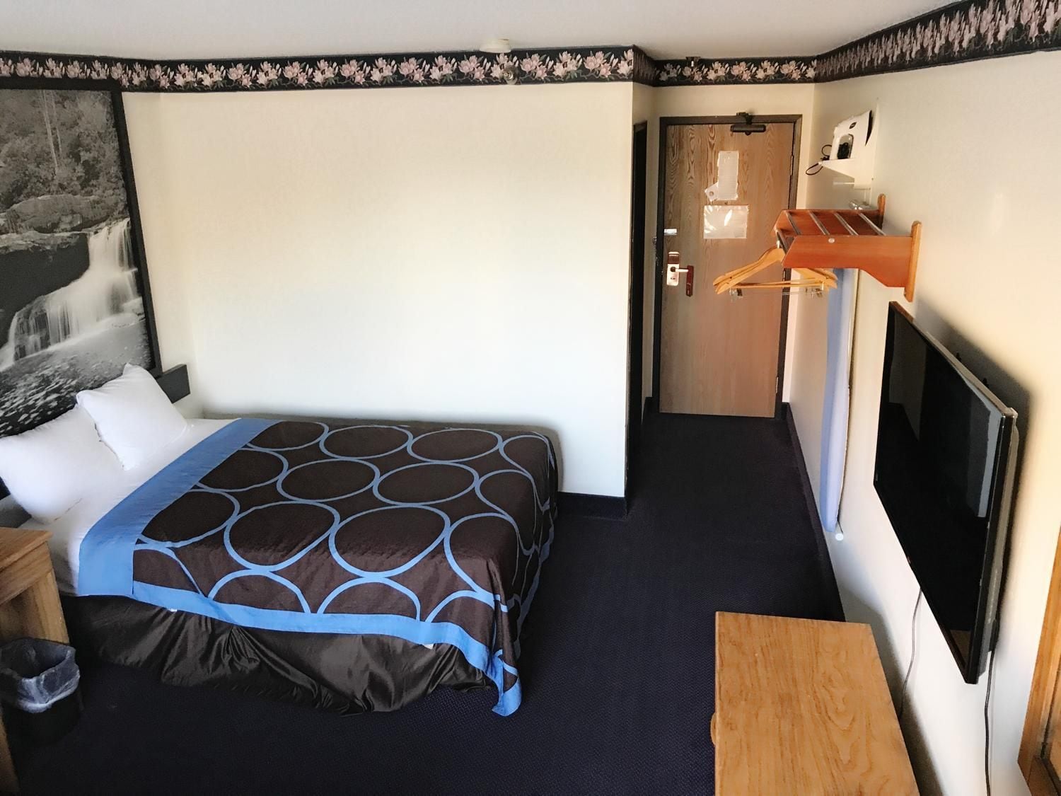 A hotel room with a bed, a television, a door, and a small table.