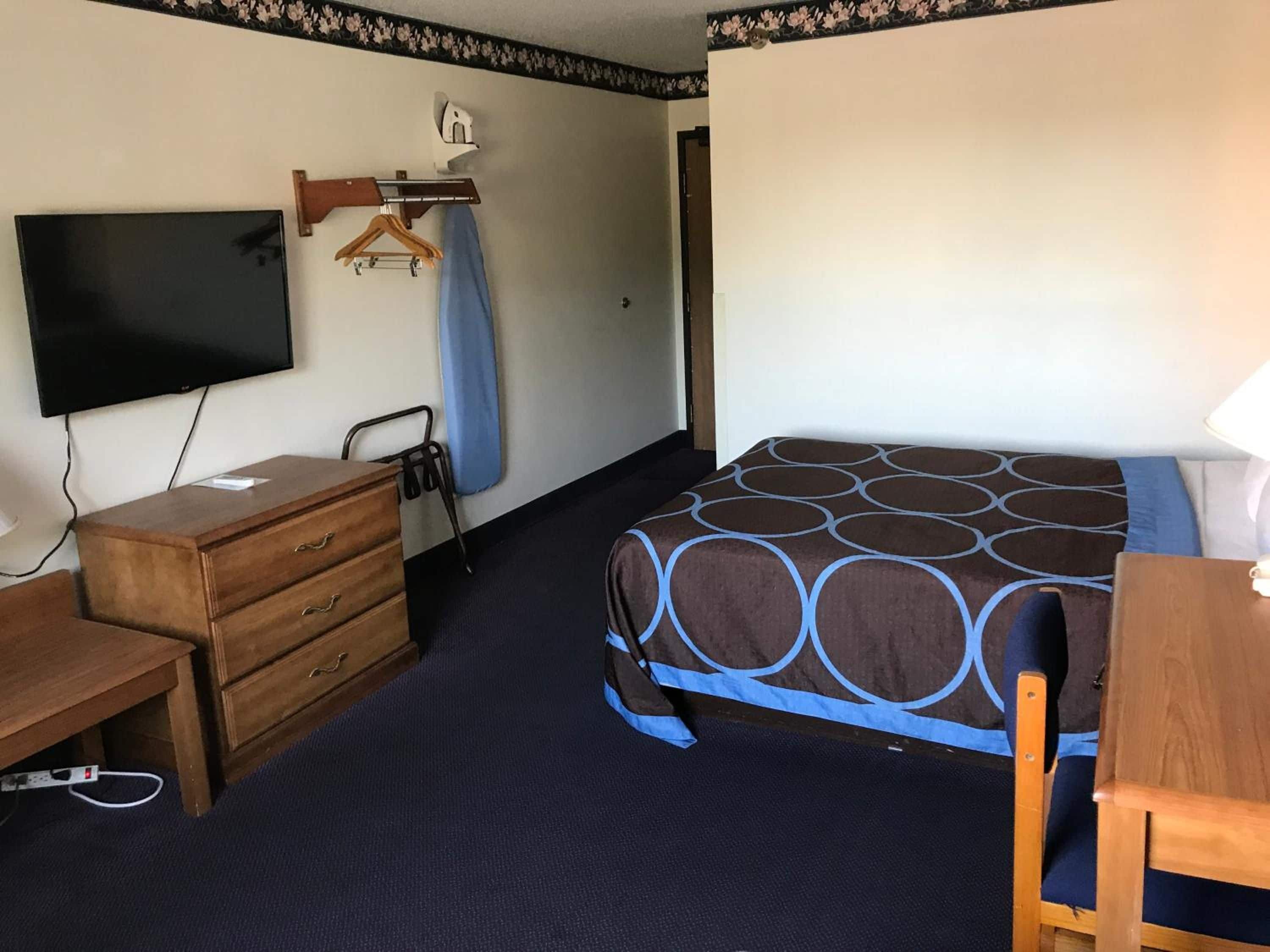 Habitación de hotel con una cama, tocador, escritorio, televisor y perchero.