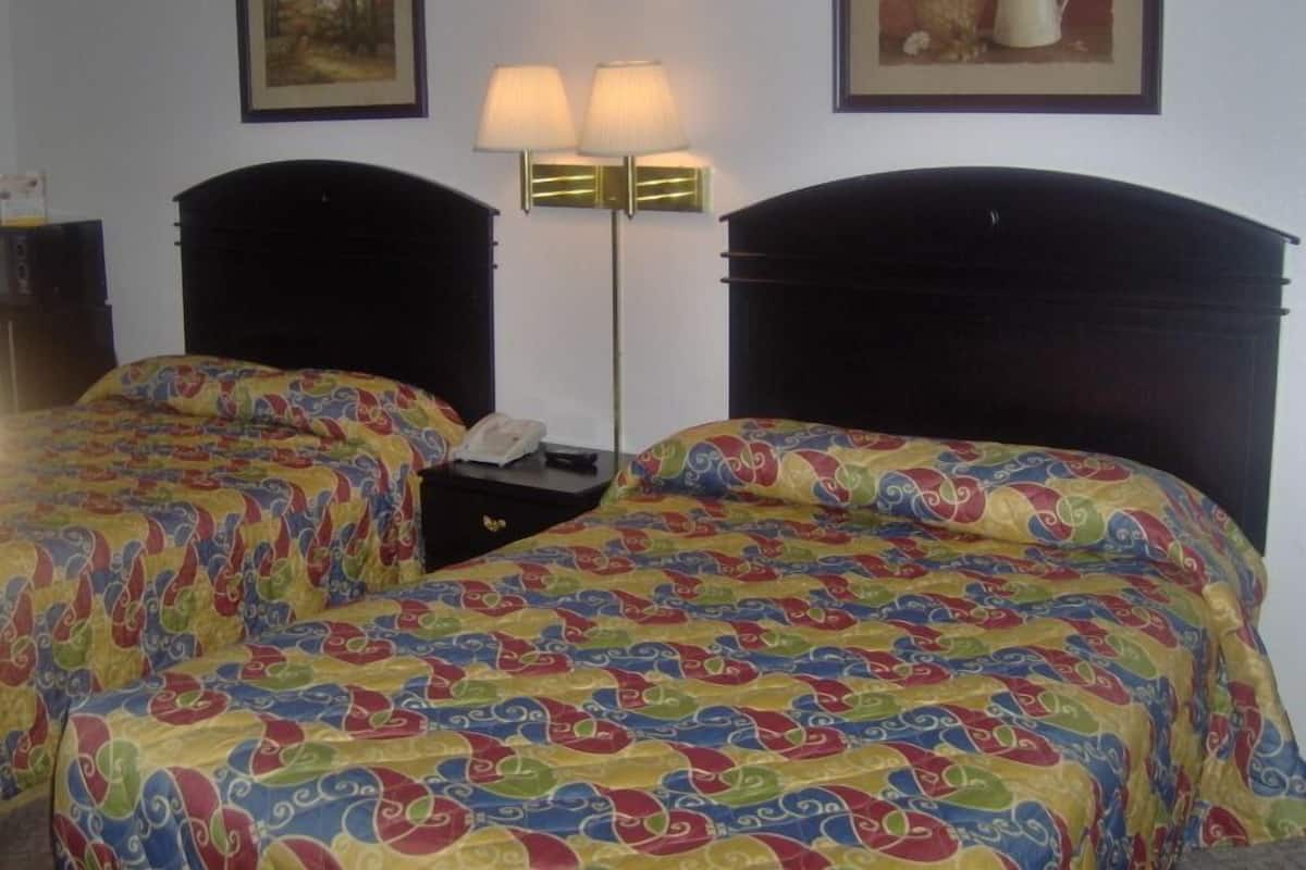 A hotel room with two beds, each with a colorful patterned bedspread, a nightstand with a lamp, and framed artwork on the walls.