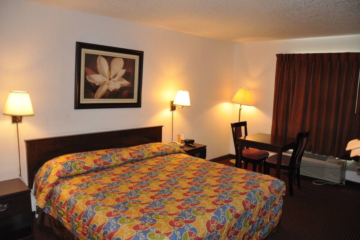 A hotel room with a large bed, two bedside lamps, a desk with a chair, and a framed picture on the wall.