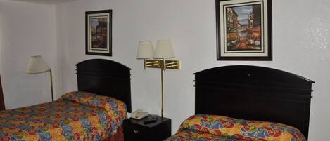 Una habitación de hotel con dos camas, una mesita de noche, una lámpara y dos cuadros en la pared.