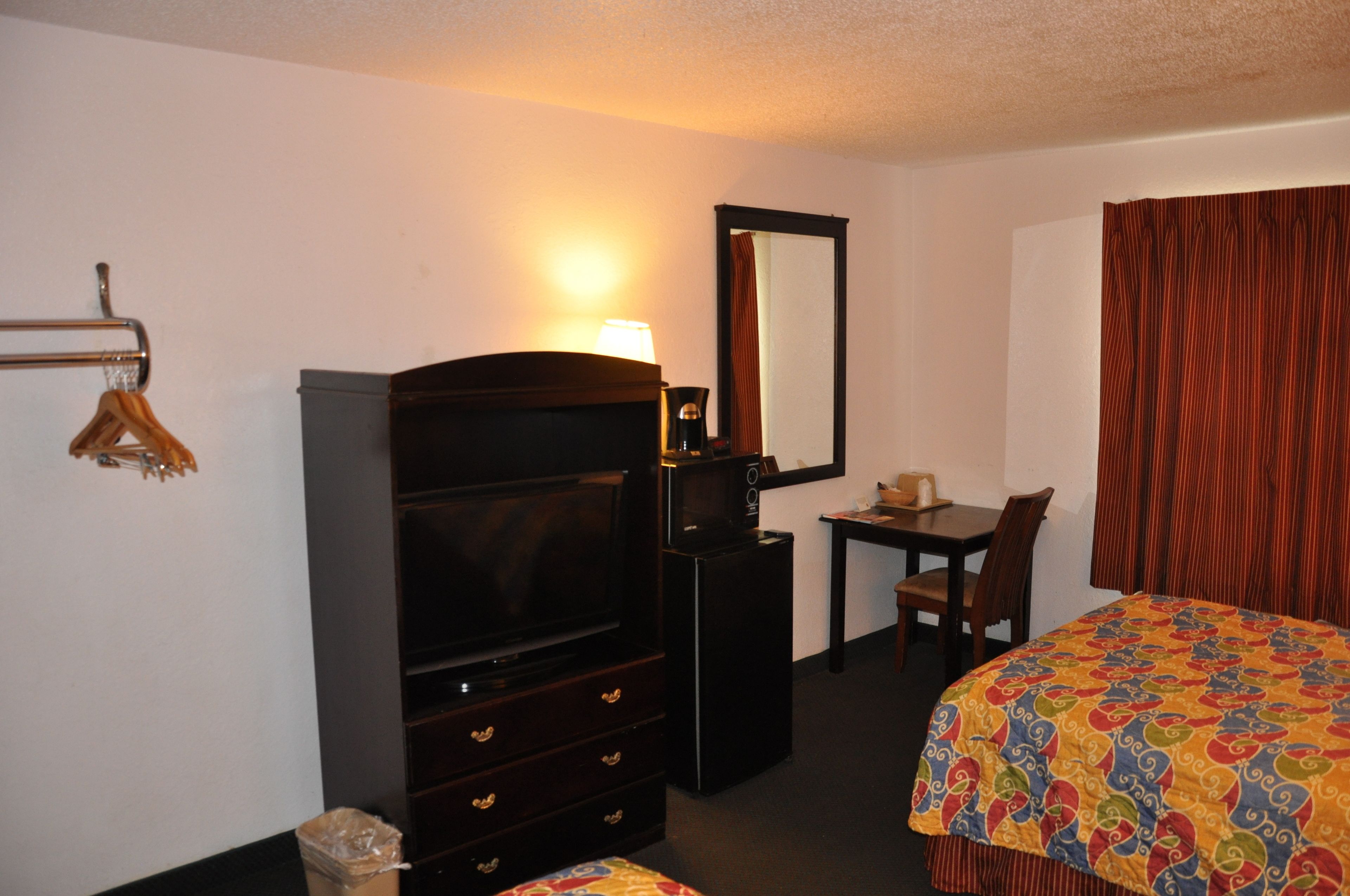 A hotel room with a bed, a desk with a chair, a television, a dresser, and a mirror.