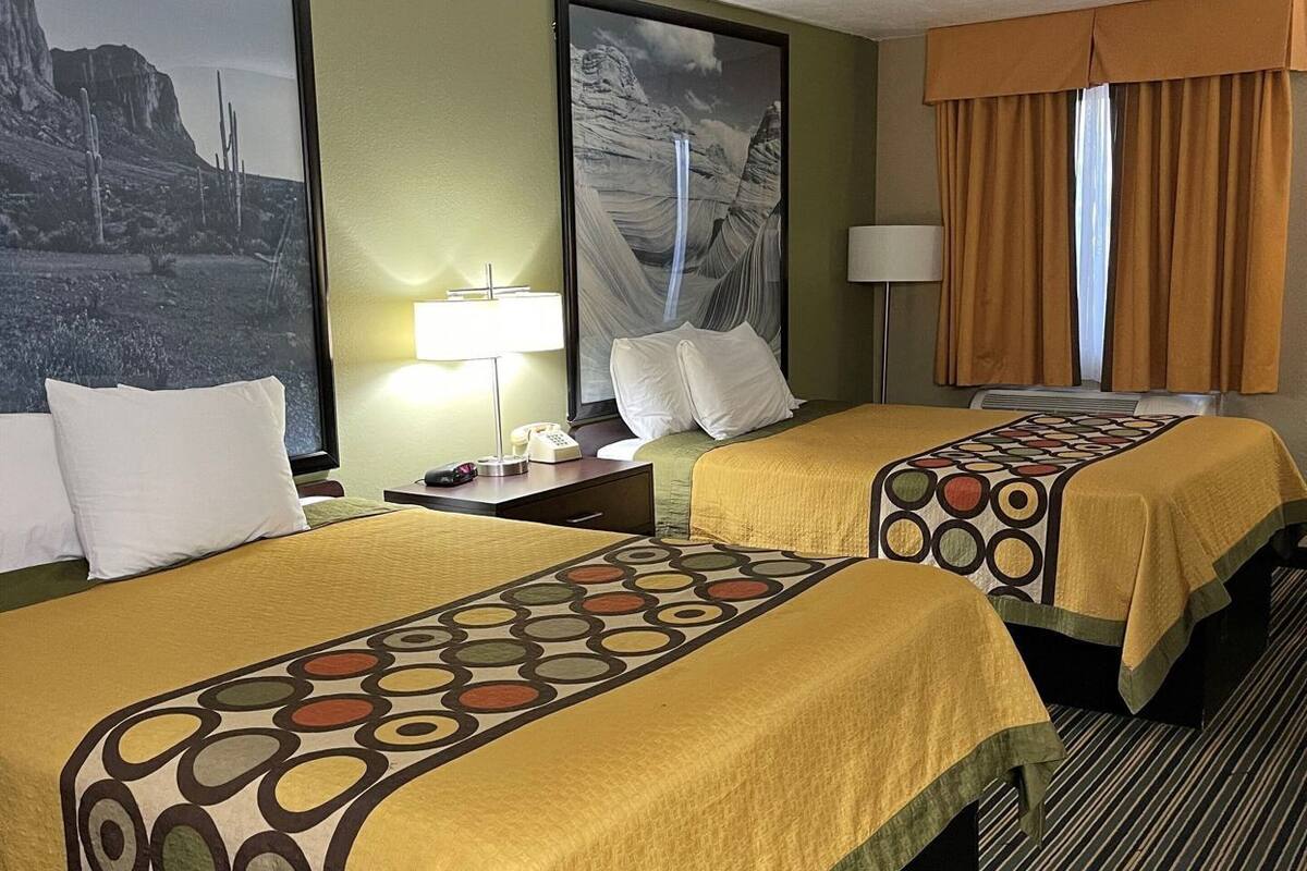 Hotelkamer met twee bedden, een groot gepresenteerd kunstwerk van een woestijnlandschap, een lamp en een raam met gordijnen.