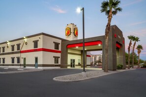 A hotel entrance with a red and beige facade, palm trees, and a clear sky.
