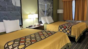 A hotel room with two beds, each with a patterned bedspread, a nightstand with a lamp, a framed picture on the wall, and a window with curtains.