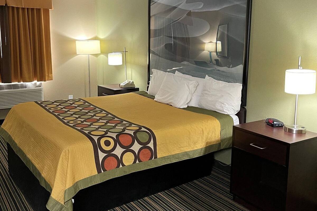 Een hotelkamer met een bed, twee nachtkastjes, een groot schilderij aan de muur en een raam met gordijnen.