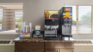 Un espace dédié au café, équipé de machines à café des marques Folgers et Florida's Natural, d'une pile de gobelets jetables, ainsi que d'un récipient contenant des dosettes de café et des sachets de sucre.