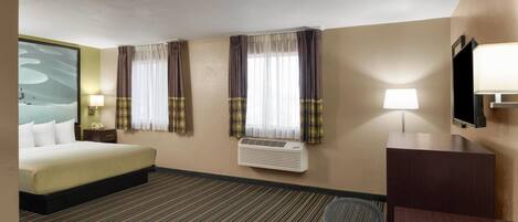 Habitación de hotel con cama, escritorio, silla, televisor y ventana con cortinas.