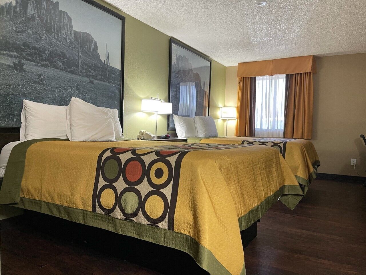 A hotel room with two beds, each with a patterned bedspread, a nightstand, a lamp, and a large framed picture on the wall.