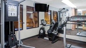Ett gym med träningsutrustning, ett löpband och en TV som är monterad på väggen.
