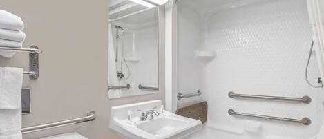 A bathroom with a sink, mirror, towel rack, and a walk-in shower with grab bars.